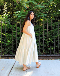 Woman wearing the Verano Dress sewing pattern by Christine Haynes. A sleeveless dress pattern made in linen, cotton or lawn fabrics, featuring a two-tier midi length full gathered skirt, in seam pockets and scoop neckline.