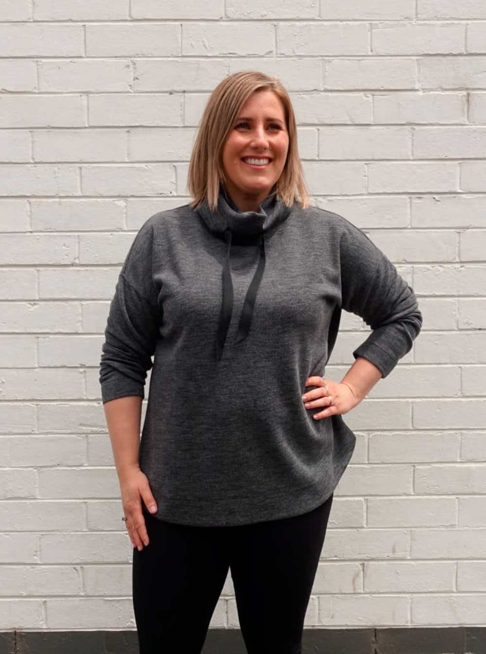 Woman wearing the Verity Knit Top sewing pattern from Style Arc on The Fold Line. A top pattern made in sweater knit, rugby or fleece fabrics, featuring a funnel neck with drawstring, extended shoulder line, boxy shape, slimline long sleeves, slightly sco