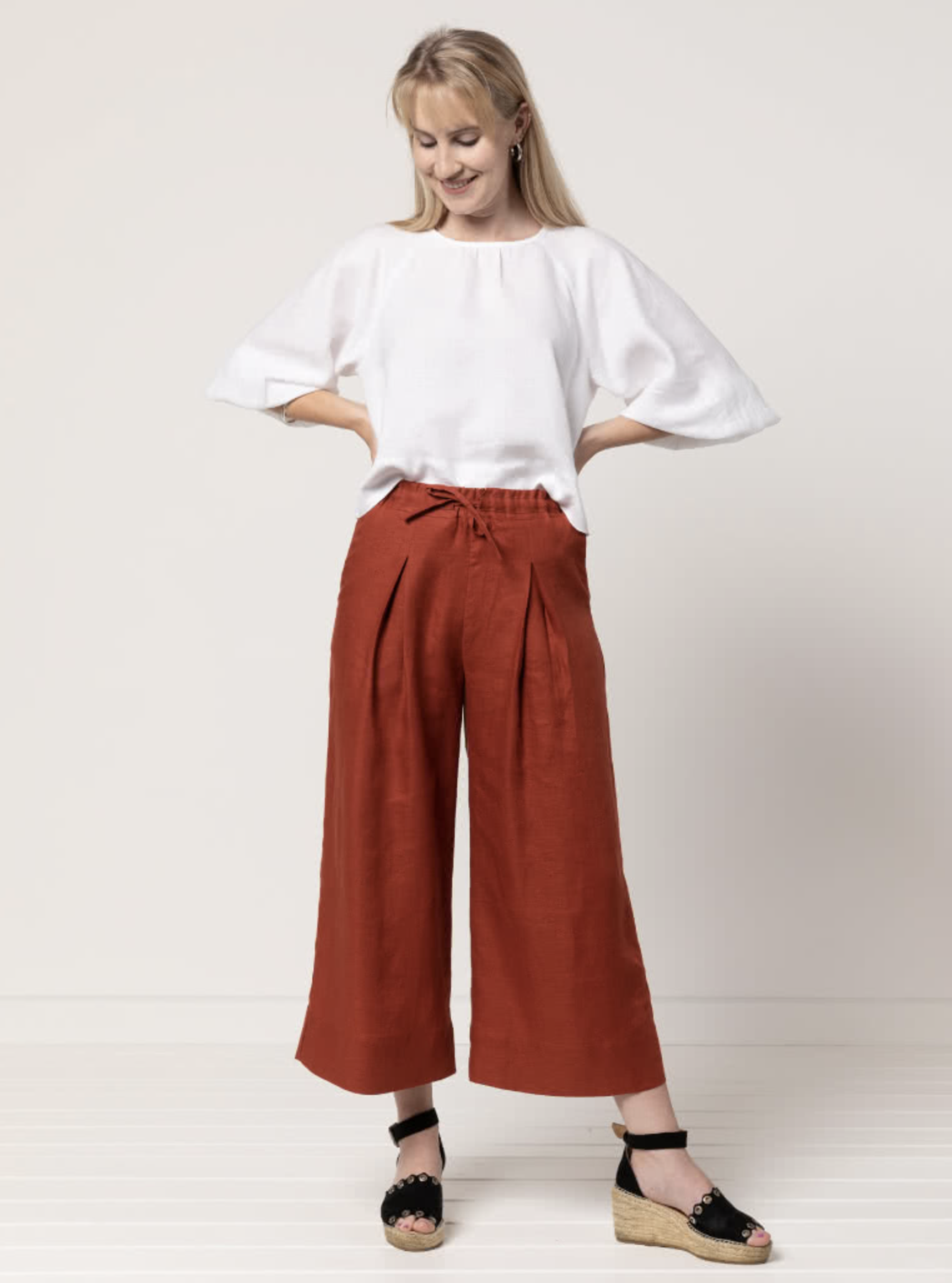 Woman wearing the Milan Woven Pant sewing pattern from Style Arc on The Fold Line. A trouser pattern made in linen or cotton fabrics, featuring a wide-leg, ankle-length, elastic waist with drawstring tie, inverted front pleats, back darts and side seam po