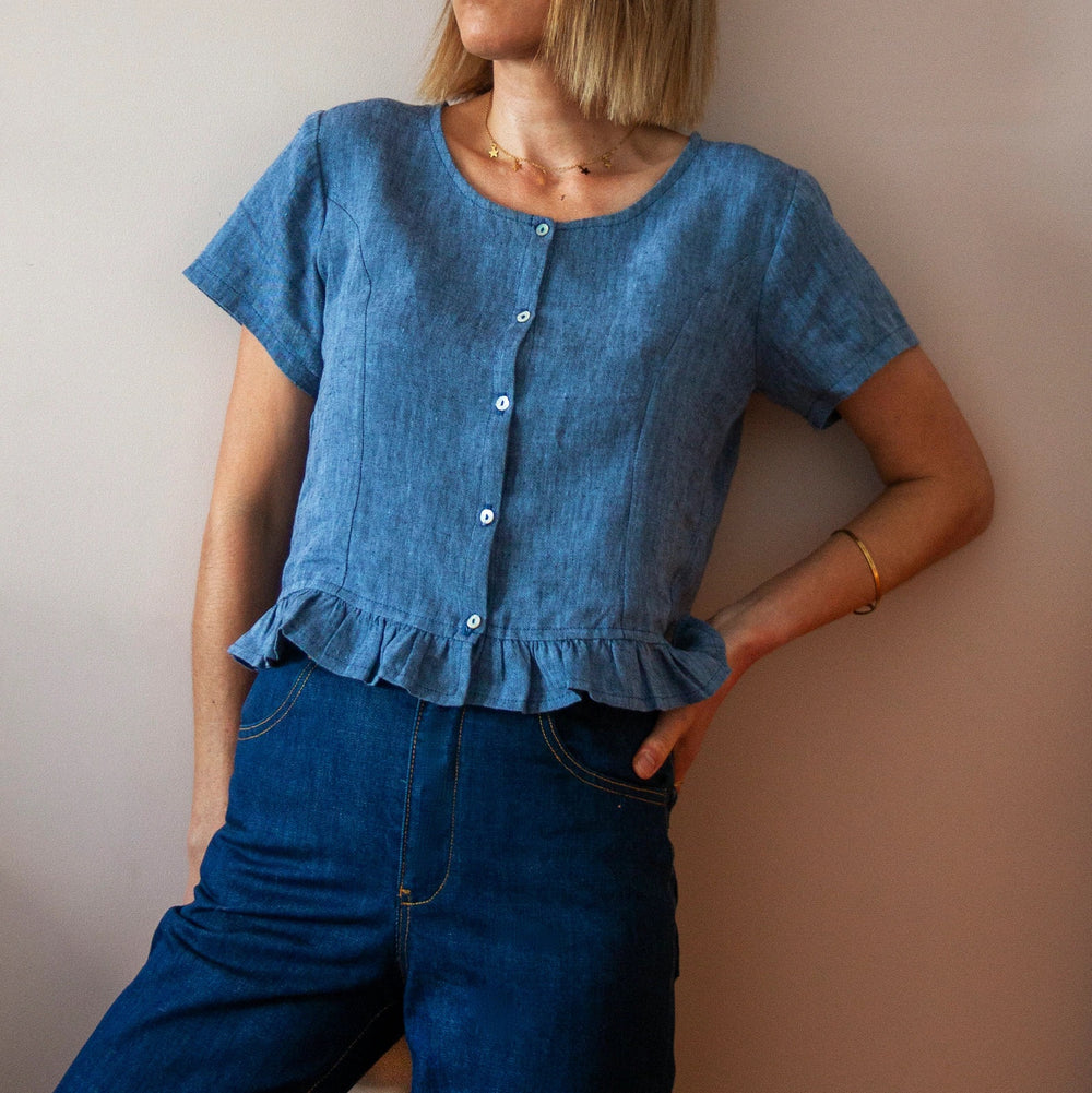 Woman wearing the Vetiver Top sewing pattern from French Navy on The Fold Line. A top pattern made in rayon, voile, lawn, shirting cotton, chambray or linen fabrics, featuring short sleeves, round neckline, narrow button stand, cropped length and ruffle h
