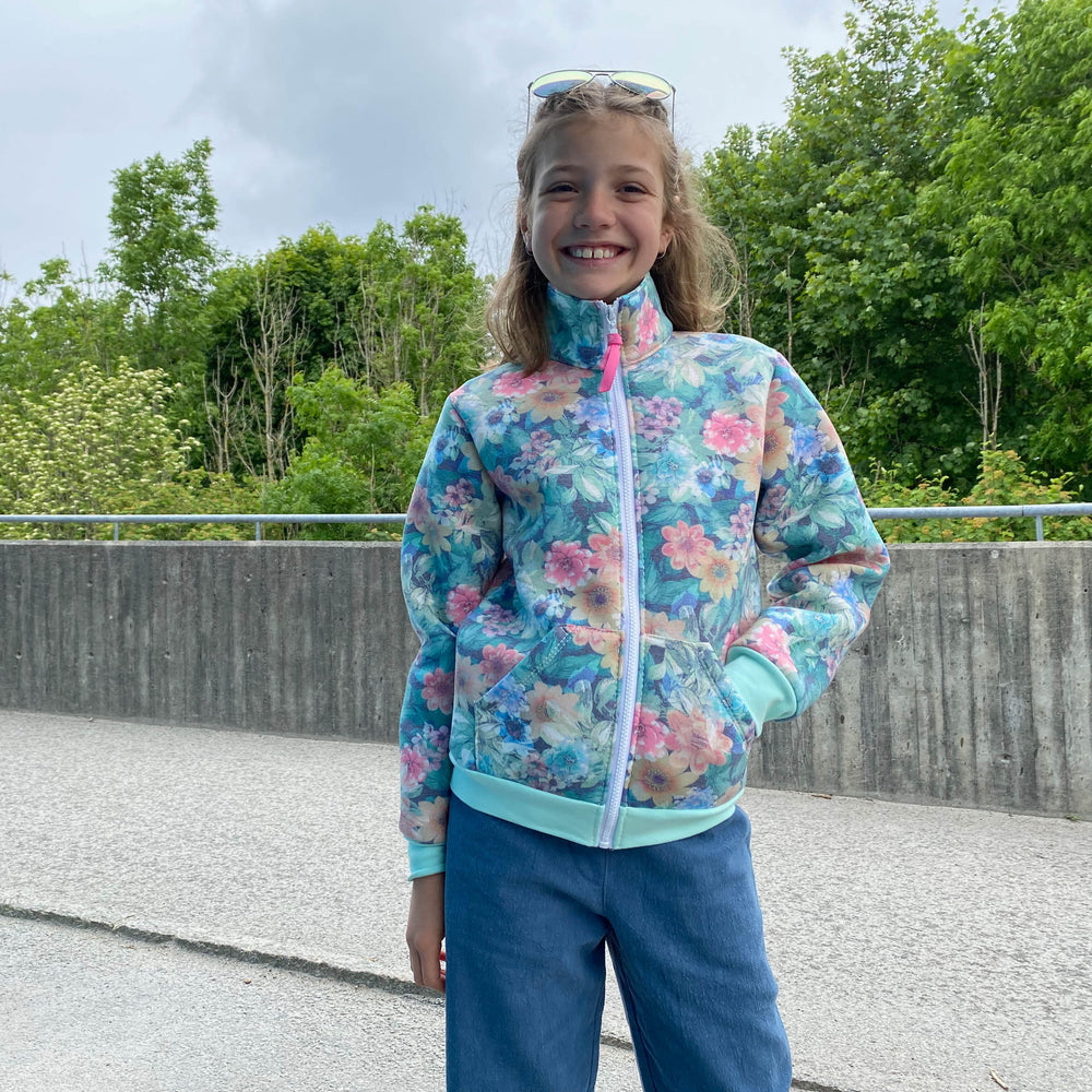 Child wearing the Children's Zipper Jacket sewing pattern from Wardrobe by Me on The Fold Line. A jacket pattern made in medium weight french terry, scuba or sweatshirt fleece fabrics, featuring a front zipper, kangaroo pockets, high funnel neck, ribbed h