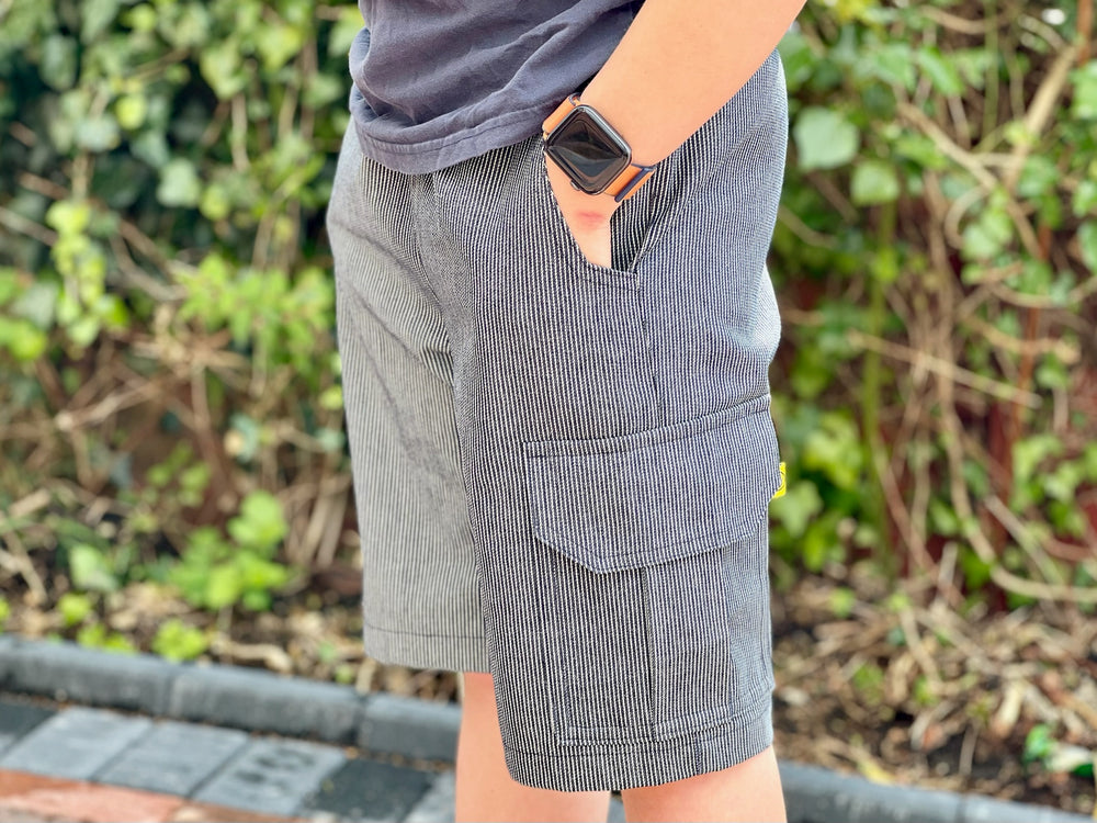 Boy wearing the Baby/Child Collector Cargo Shorts sewing pattern from Waves & Wild on The Fold Line. A shorts pattern made in twill, denim, or corduroy fabric, featuring a relaxed fit, comfortable elastic waist, patch pockets, and hip pockets.