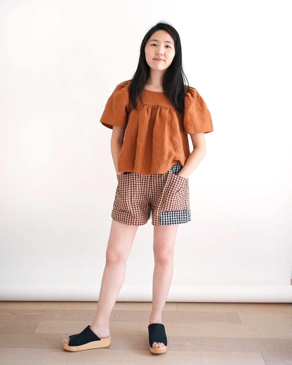 Woman wearing the Weekend Chore Shorts sewing pattern from Matchy Matchy Sewing Club on The Fold Line. A shorts pattern made in medium and bottom weigh woven fabrics, featuring a loose fit, front pockets, high-rise gathered elastic waist, and inseam front