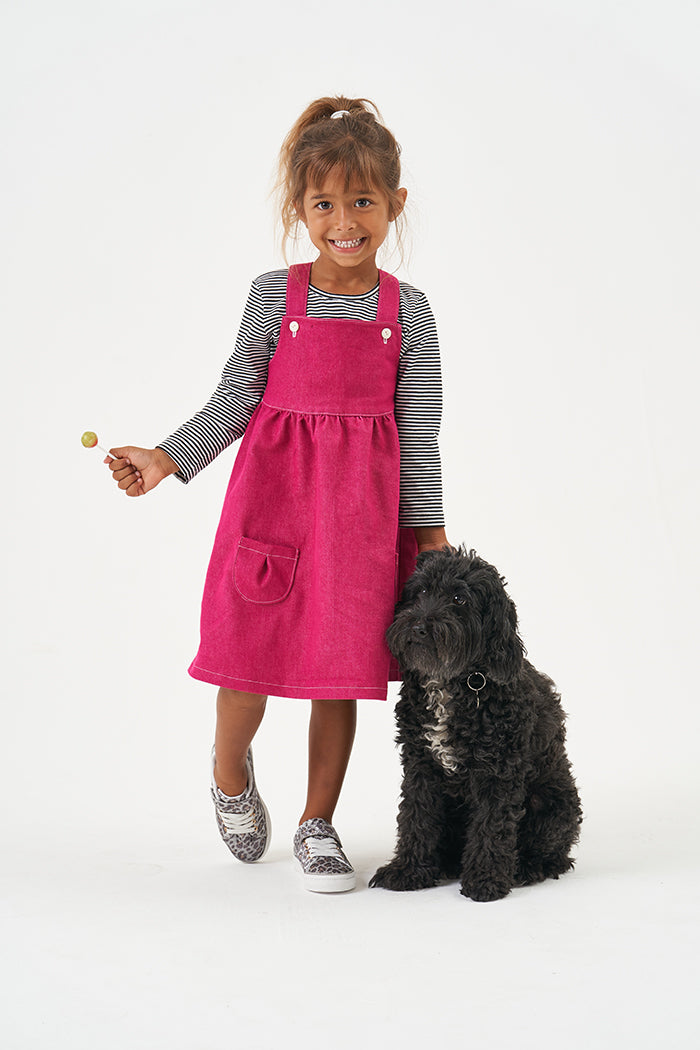 Child wearing the Baby/Child Willow Pinafore sewing pattern from Poppy & Jazz on The Fold Line. A pinafore pattern made in cotton lawn, cotton poplin, linen, denim, quilting cottons or corduroy fabrics, featuring a bib with adjustable straps, gathered ski