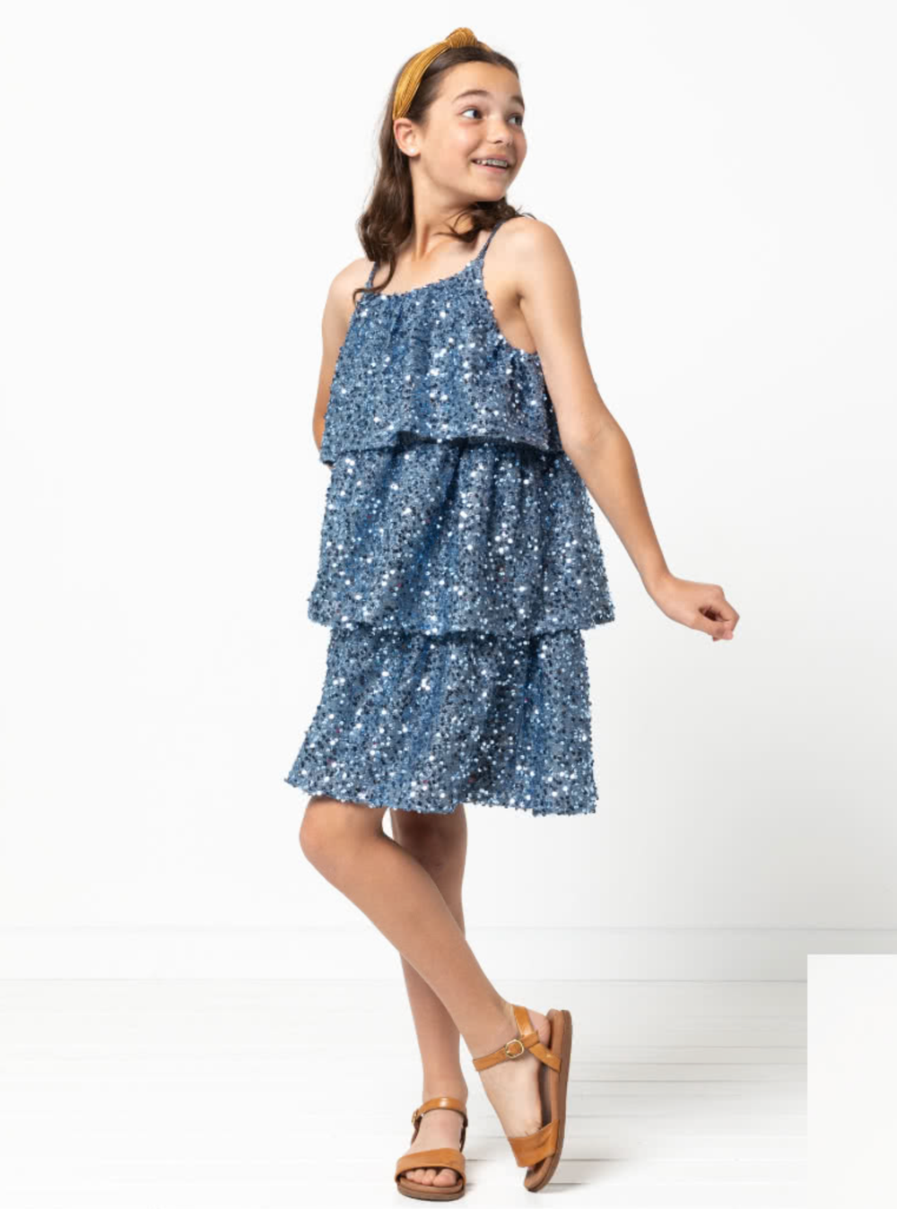 Child wearing the Child/Teen Wilma Dress sewing pattern from Style Arc on The Fold Line. A sleeveless dress pattern made in cotton, rayon, silk or linen fabrics, featuring a pull-on style, three tiers, spaghetti straps, and elastic at the underarms and ba