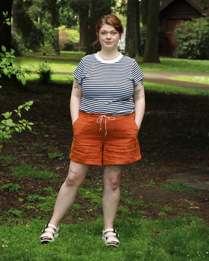 Woman wearing the Women's Bamberton Shorts sewing pattern from Thread Theory on The Fold Line. A shorts pattern made in linen, cotton, seersucker, cotton and linen blend, polyester, or nylon fabric, featuring a drawstring waistband, side seam panels, mock