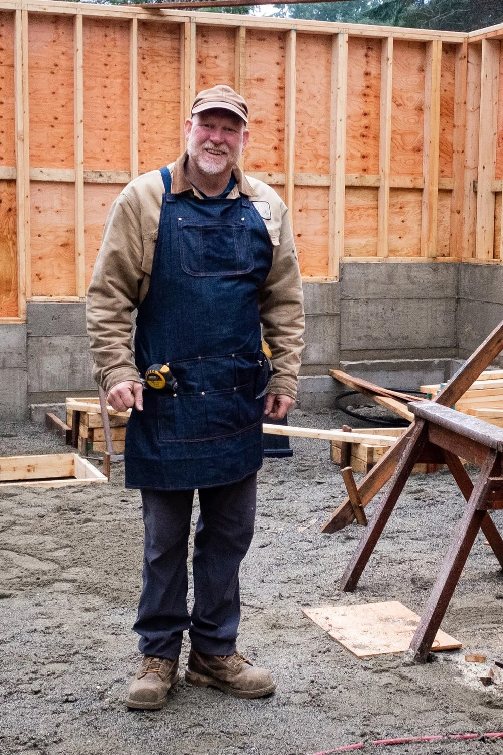 Man wearing the Woodhaven Apron sewing pattern from Thread Theory on The Fold Line. An apron pattern made in canvas, denim, linen or ticking fabrics, featuring a chest pocket with inner zipped pocket, divided pleated hip pockets, straps that fasten at the