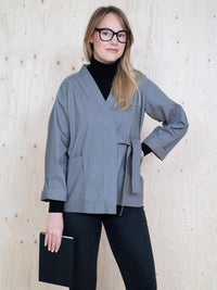 Woman wearing the Wrap Jacket sewing pattern from The Assembly Line on The Fold Line. A jacket pattern made in cotton twill, denim or lightweight canvas fabrics, featuring large pockets, full length sleeves turned back, crossover front with matching fabri