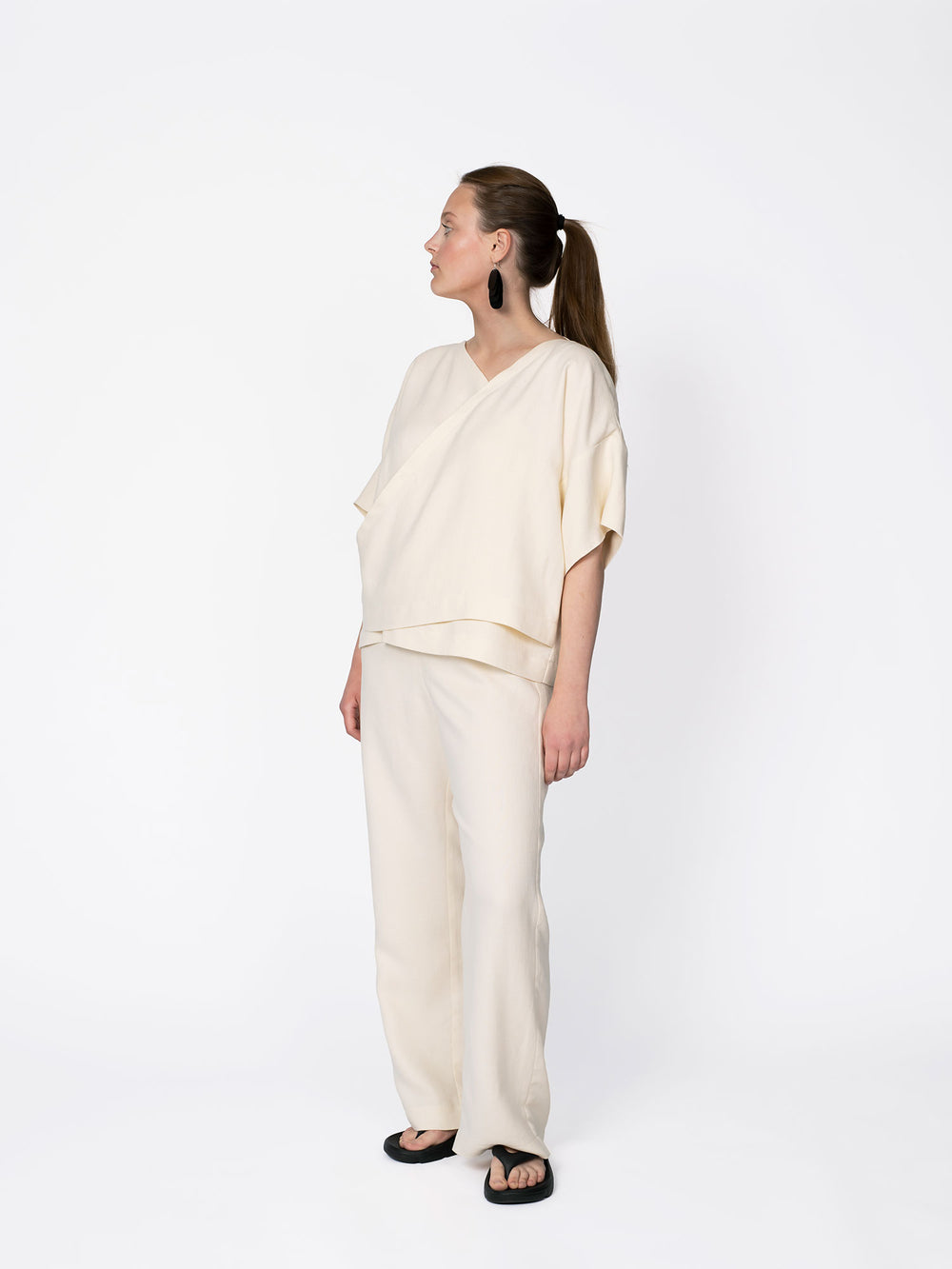 Woman wearing the Wrap Top sewing pattern from The Assembly Line on The Fold Line. A shirt pattern made in cotton, linen, viscose, wool or blends, and lightweight twill fabrics, featuring a relaxed boxy fit, two uneven overlapping shaped fronts, asymmetri