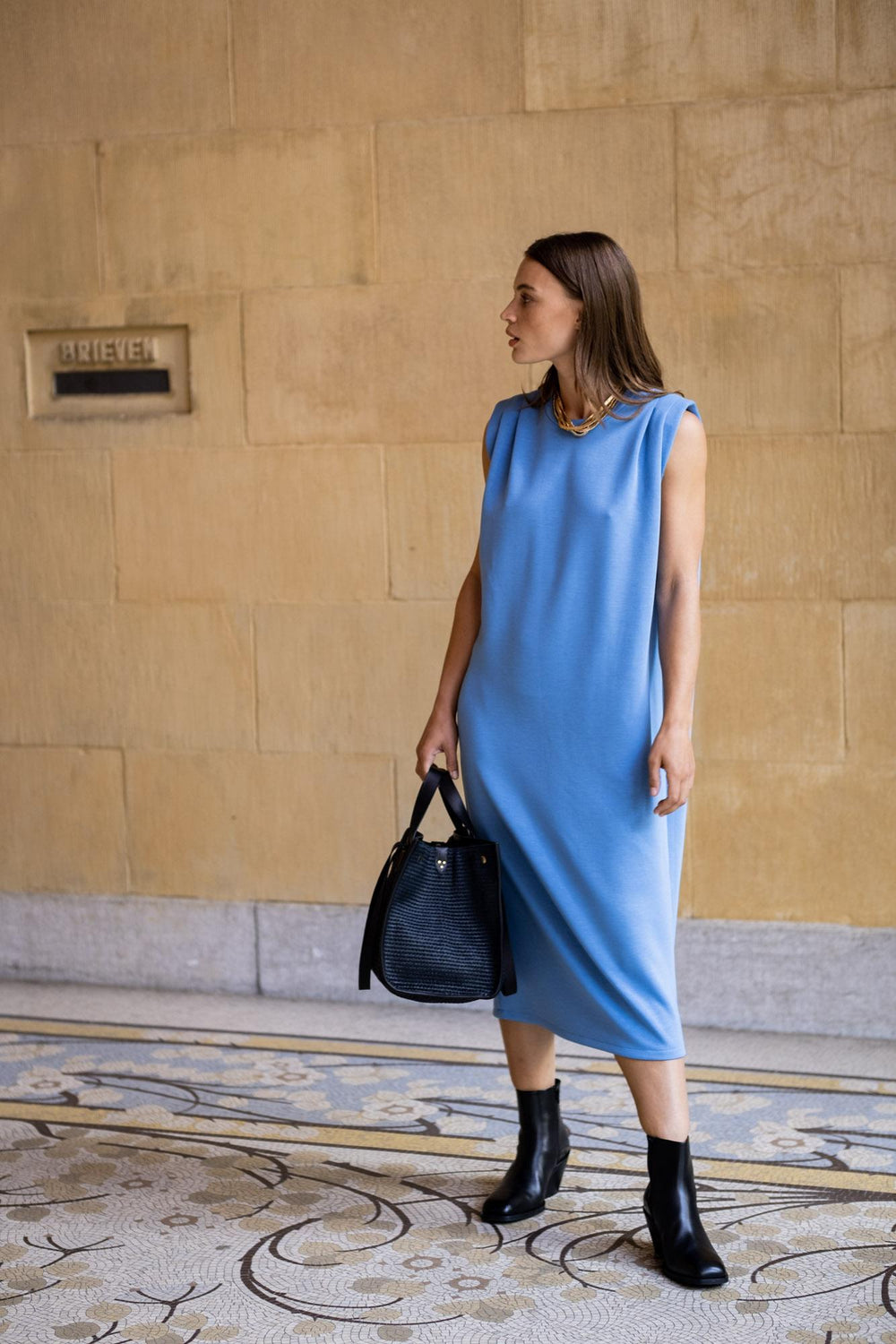 Woman wearing the Yushu Dress sewing pattern from Fibre Mood on The Fold Line. A dress pattern made in knit fabrics, featuring shoulder pleats, shoulder pads, sleeveless, relaxed straight fit and midi length.