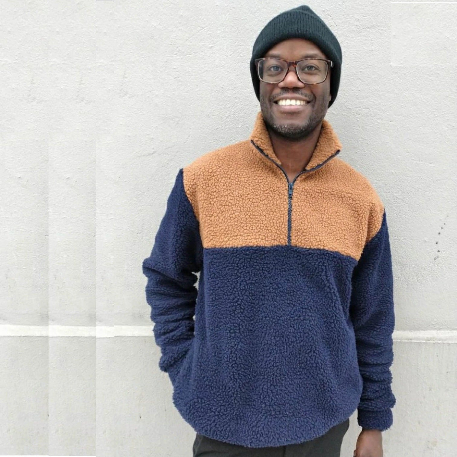 Man wearing the Men's Zip-up Sweater sewing pattern from Wardrobe by Me on The Fold Line. A sweater pattern made in fleece, French terry or fluffy teddy fleece fabrics, featuring a zipper from the neck to the chest, roomy fit, dropped shoulders, side pock