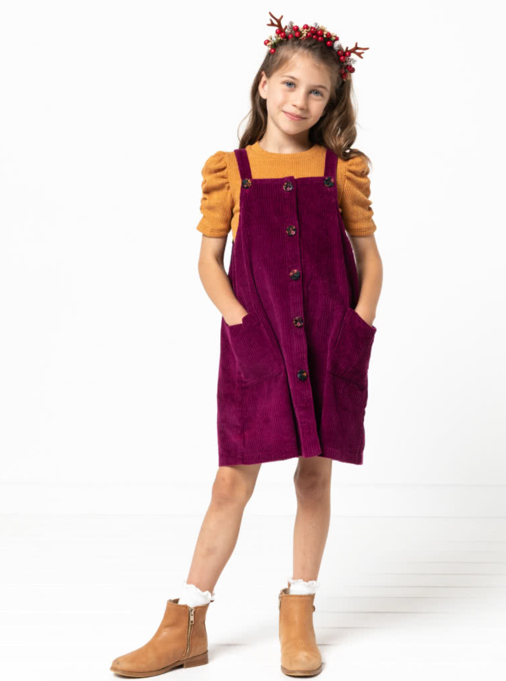 Child wearing the Baby/Child Zoe Pinafore sewing pattern from Style Arc on The Fold Line. A pinafore dress pattern made in denim, corduroy, cotton or ponte fabrics, featuring a slight A-line silhouette, button through front, adjustable shoulder straps, tw