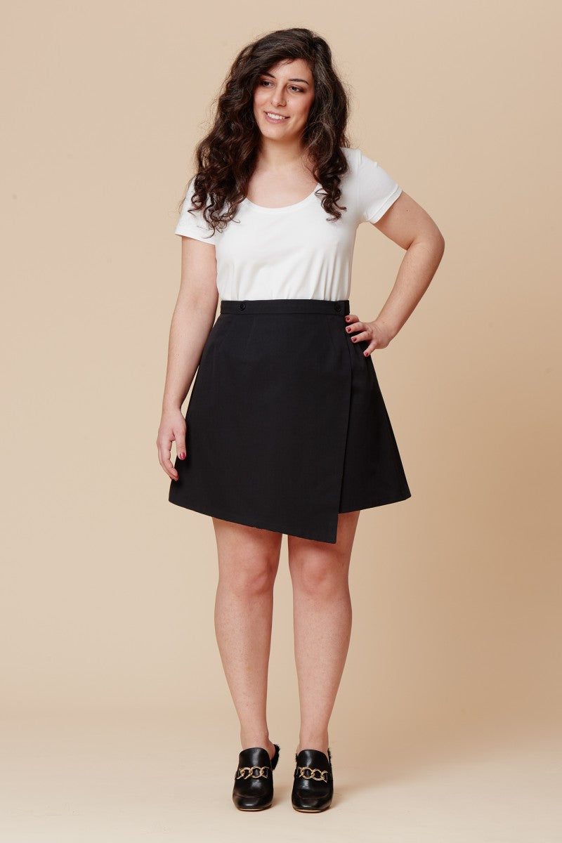 Woman wearing the Agave Skirt sewing pattern by Deer and Doe. An A-line wrap skirt pattern made in lightweight twill, linen, chambray or cotton sateen fabric featuring a high waist, with asymmetrical panels and button closure.