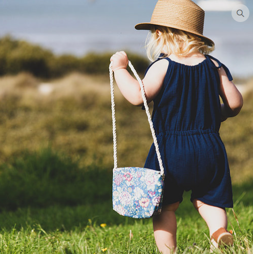 Child wearing the Child/Baby Bloomer Romper sewing pattern from Elemeno Patterns on The Fold Line. A romper pattern made in woven or knit fabrics, featuring tie shoulder straps, sleeveless, round neck, elasticated waist, roomy fit and elasticated above kn