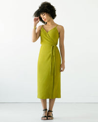 Woman wearing the Calvin Wrap Dress sewing pattern by True Bias. A sleeveless dress pattern made in linen, chambray, rayon or cotton fabric featuring a low V-neck, adjustable shoulder straps and waist tie closure.