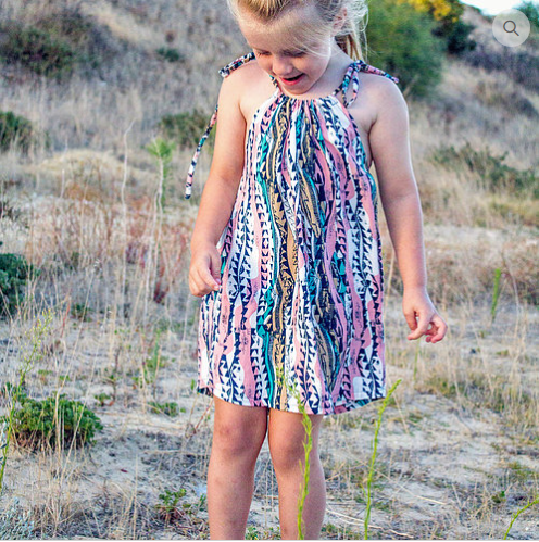 Child wearing the Child/Baby Cami Dress sewing pattern from Elemeno Patterns on The Fold Line. A sleeveless sundress pattern made in gauze, light linen, cotton knit or rayon fabrics, featuring spaghetti tie shoulder straps, gathered at the neck and loose 