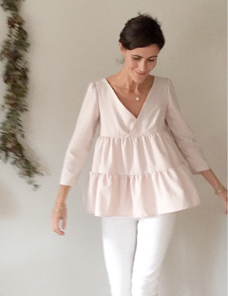 Woman wearing the Eugénie Blouse sewing pattern by Atelier Scammit. A blouse pattern made in very light to medium batiste, crepe, light denim or flannel fabrics, featuring ruffled sleeves, wrap V-neckline, smocking and tiers.