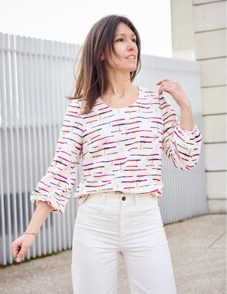Woman wearing the Hilda Blouse sewing pattern from Atelier Scämmit on The Fold Line. A blouse pattern made in batiste, crepe, or double gauze fabrics, featuring a round neck, bracelet length puff sleeves with elastic cuff and relaxed fit.