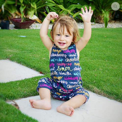 Child wearing the Child/Baby Racerback Romper sewing pattern from Elemeno Patterns on The Fold Line. A romper pattern made in stretch fabrics, featuring knee length legs, round neck, deep armholes, relaxed fit, wide shoulder straps with snap closure and s