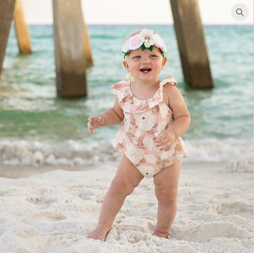 Child wearing the Child/Baby Ruffle Romper sewing pattern from Elemeno Patterns on The Fold Line. A romper pattern made in woven or knit fabrics, featuring a round neckline with ruffle, sleeveless, roomy fit, elasticated knicker legs and snap crotch closu