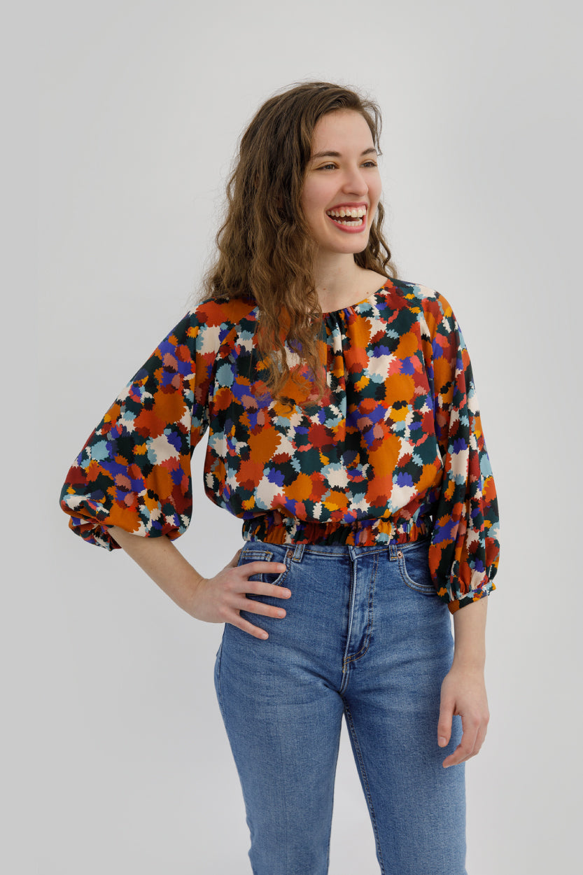 Woman wearing the Whitcomb Top sewing pattern from Sew Love Patterns on Fold Line. A top pattern made in cotton, linen, viscose, cupro, crepe and rayon fabrics, featuring ¾ length sleeves with gathered cuffs, hip length, and round neckline with gathered f