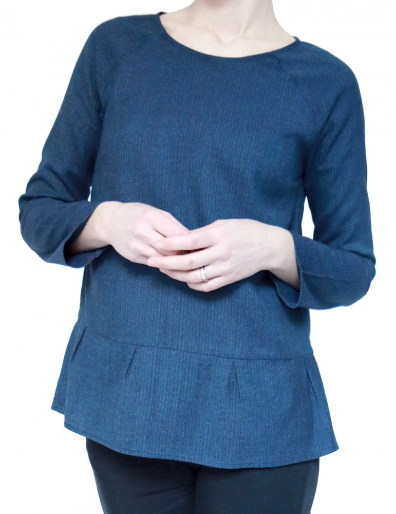 Woman wearing the Stockholm Blouse sewing pattern by Atelier Scammit. A blouse pattern made in very light to medium weight jersey (or woven fabric, one size larger) fabrics, featuring long, raglan sleeves, round neck and a back button and loop closure.