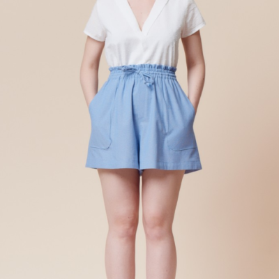 Woman wearing the Goji Shorts sewing pattern by Deer and Doe. A shorts pattern made in chambray, rayon twill, batiste or linen fabric featuring a high, elasticated paper bag waist, drawstring and patch pockets.