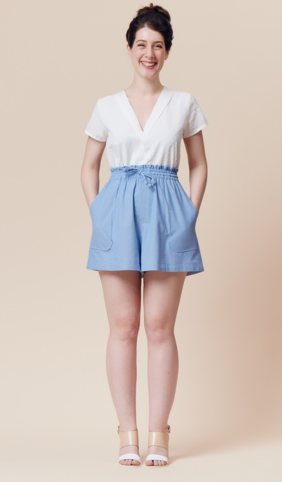 Woman wearing the Goji Shorts sewing pattern by Deer and Doe. A shorts pattern made in chambray, rayon twill, batiste or linen fabric featuring a high, elasticated paper bag waist, drawstring and patch pockets.
