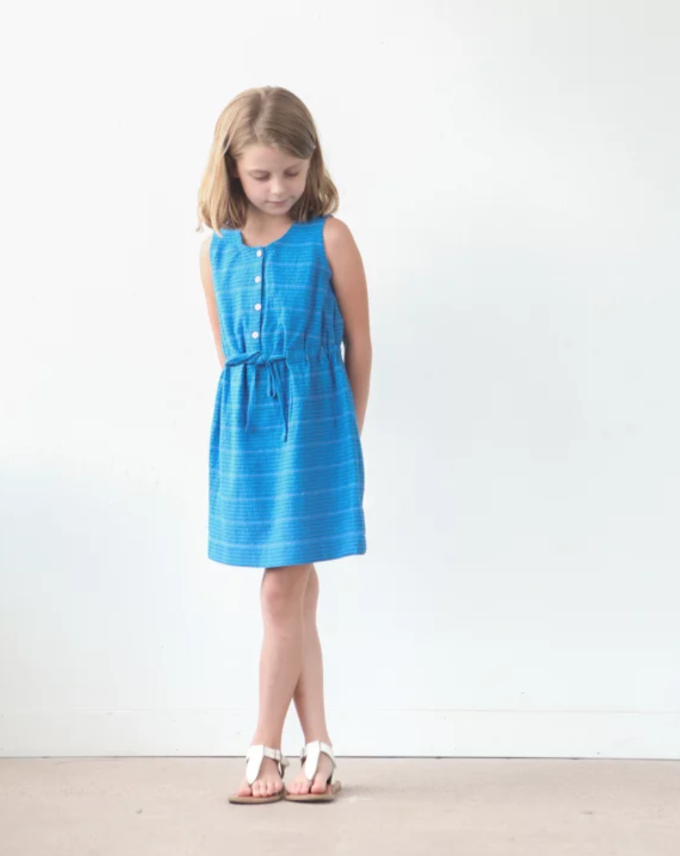 Girl wearing the Mini Southport Dress sewing pattern by True Bias. A sleeveless, tank style dress pattern made in cotton voile, cotton, linen or double gauze fabric featuring a front button opening and combination elastic and drawstring waist.
