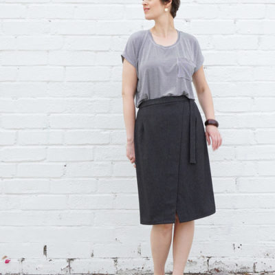 Woman wearing the Nita Wrap Skirt sewing pattern from Sew DIY on The Fold Line. A wrap skirt pattern made in cotton, linen, twill, poplin, sateen, wool crepe, corduroy or denim fabrics, featuring a fitted silhouette, angled front, knee length finish, waist darts and fabric waist tie closure.
