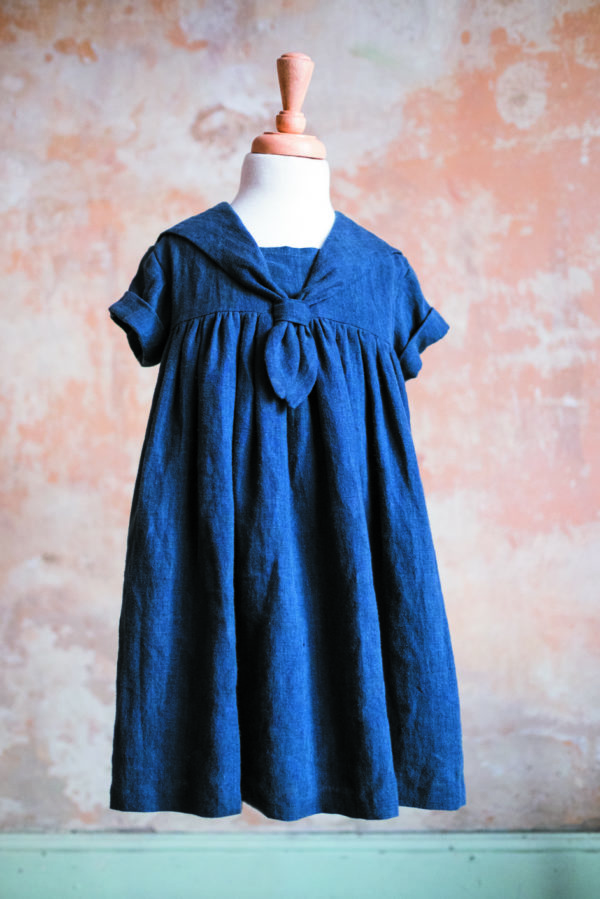 The Child’s Skipper Dress sewing pattern by Merchant and Mills. A sailor dress pattern made in denim, cotton chambray, linen or lightweight wool fabric featuring dropped shoulders, short sleeves with rolled cuffs, gathered yoke and neck tie.
