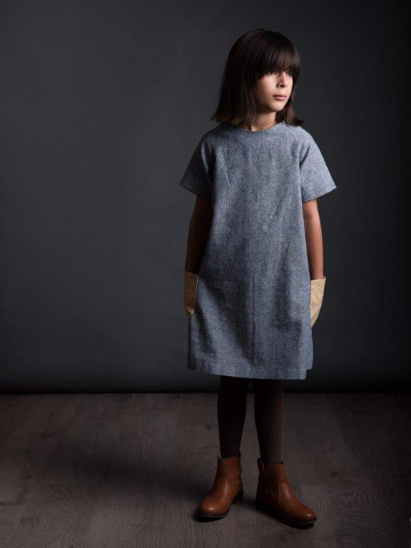 Child wearing Children's Raglan Dress sewing pattern from The Avid Seamstress on The Fold Line. A dress pattern made in light to medium weight fabrics, featuring a knee length hem, patch pockets, round neck, short raglan sleeves and invisible back zip closure.