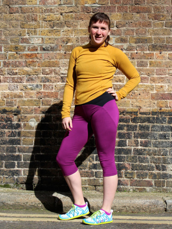 Woman wearing the Steeplechase Leggings sewing pattern from Fehr Trade on The Fold Line. An athletic leggings pattern made in lycra fabrics, featuring no inseams, curved outer seams, separate yoke pieces, optional hidden back pocket, elasticated waistband, and capri length.