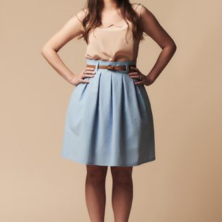 Woman wearing the Chardon Skirt sewing pattern by Deer and Doe. A knee length skirt pattern made in lightweight twill, linen, denim, chambray or cotton sateen fabric featuring a high waist, inverted box pleats, and belt loops.