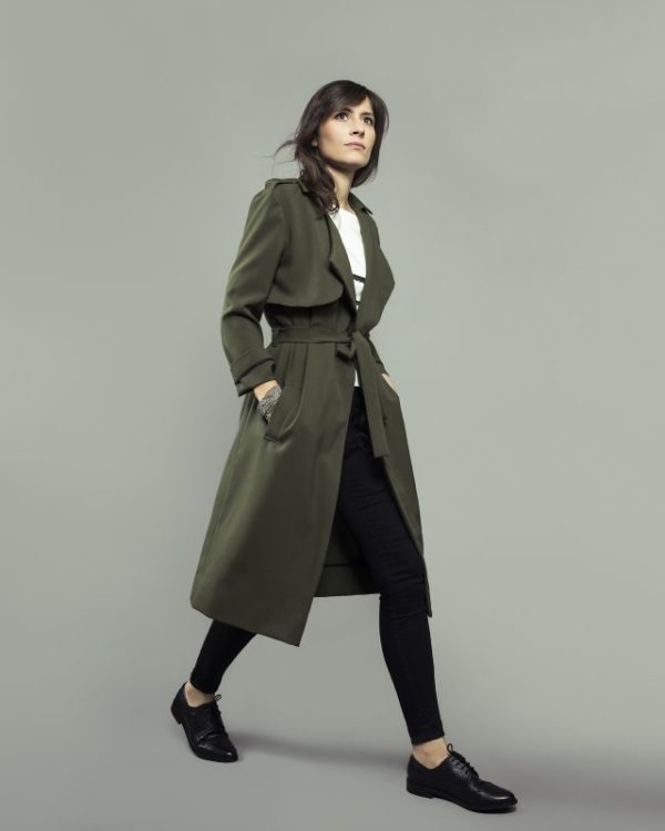 Woman wearing the Londres Trench Coat sewing pattern from Orageuse on The Fold Line. A trench coat pattern made in lyocell, viscose, microfiber or gabardine fabrics, featuring a tailored collar, wide lapels, asymmetrical shoulder flap and shoulder tabs, midi length finish, self-fabric tie belt closure and front pockets.