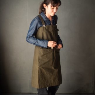Woman wearing the Victor Apron sewing pattern by Merchant and Mills. An apron pattern made in oilskin, denim, cotton canvas or drill fabric featuring a large divided waist pocket with scissor holder, top pocket and cross back for comfort.
