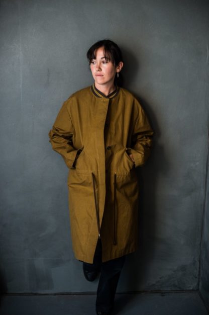 Woman wearing the TN31 Parka sewing pattern by Merchant and Mills. A coat pattern made oilskin, tweed, cotton drill, linens or waterproof cotton featuring side pockets, long length, front pockets, back vent and front button closure.