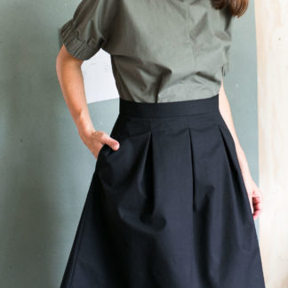 Woman wearing the Three Pleat Skirt sewing pattern by The Assembly Line. A pleated skirt pattern made in denim, cotton twill or canvas fabric featuring a right side pocket, and left side zipper opening.