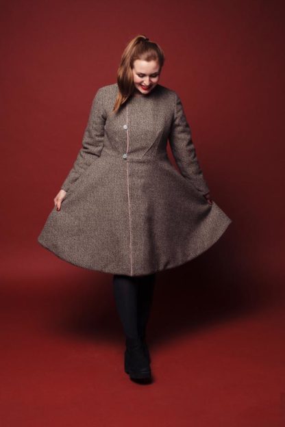 Woman wearing the Ingvild Coat sewing pattern from Melilot on The Fold Line. A reversible coat pattern made in cotton, linen or wool fabrics, featuring an asymmetric button and loop closure, round neckline without collar, side seam pockets, front bodice darts and knee length hem.