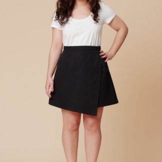 Woman wearing the Agave Skirt sewing pattern by Deer and Doe. An A-line wrap skirt pattern made in lightweight twill, linen, chambray or cotton sateen fabric featuring a high waist, with asymmetrical panels and button closure.