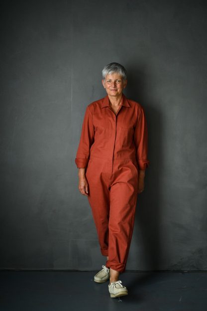 Woman wearing the Thelma Boilersuit sewing pattern from Merchant and Mills on The Fold Line. A boilersuit pattern made in twill, denims, linens or cotton poplin fabrics, featuring a loose fit, front and back patch pockets, front pockets, back yoke, two piece collar, cuff and button sleeve closure, full length sleeves, centre front zip closure and adjustable side waist with tab and button.