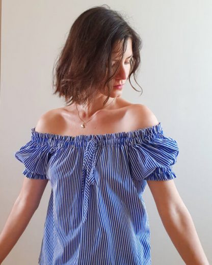 Woman wearing the Polaris Top sewing pattern by French Poetry. A top pattern made in cotton lawn, shirting, viscose, silk crepe, twill or challis fabrics, featuring an off-the-shoulder peasant top with gathers on the neckline and arms, the gathers are made using elastic casings and an optional bow that can be added to the front.