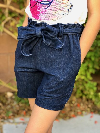 Child wearing the Lola Shorts sewing pattern from 5 out of 4 Patterns on The Fold Line. A shorts pattern made in rayon challis, crepe, satin charmeuse, peach skin or some poly blend fabrics, featuring a paper-bag waist with self-fabric tied belt, relaxed fit and slash pockets.