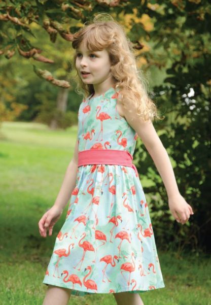 Child wearing the Baby/Child Dorothy Dress sewing pattern by Bobbins and Buttons. A sleeveless dress pattern made in craft weight cottons, cotton blends, lawn or broadcloth fabrics, featuring a gathered skirt fastened with a centre back zip and a sash tie at the waist.