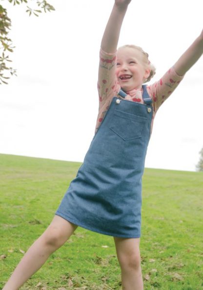 Child wearing the Baby/Child Mary Dress sewing pattern by Bobbins and Buttons. A pinafore dress pattern made in denim, corduroy, needlecord, cotton or cotton blend fabrics, featuring an A-line silhouette, pockets and shoulder straps.