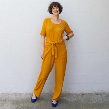 Woman wearing showing the Dana Jumpsuit sewing pattern from Sew DIY on The Fold Line. A jumpsuit pattern made in linen, chambray, cotton lawn, poplin, rayon, tencel or crepe de chine fabrics, featuring a front waist tie that creates subtle shaping, scoop neck, set-in elbow-length sleeves, invisible back zipper and high curved back neckline.
