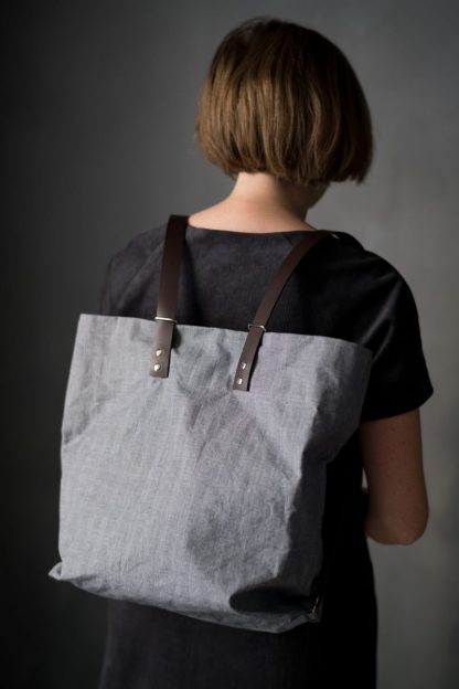 Woman wearing The Costermonger Tote sewing pattern from Merchant & Mills on The Fold Line. A tote bag pattern made in oilskin, dry oilskin, mid-heavy weight cotton canvas, drill or mid weight denim fabrics, featuring fixed length shoulder straps that are attached to the outside of the bag and featuring no zips or pockets.