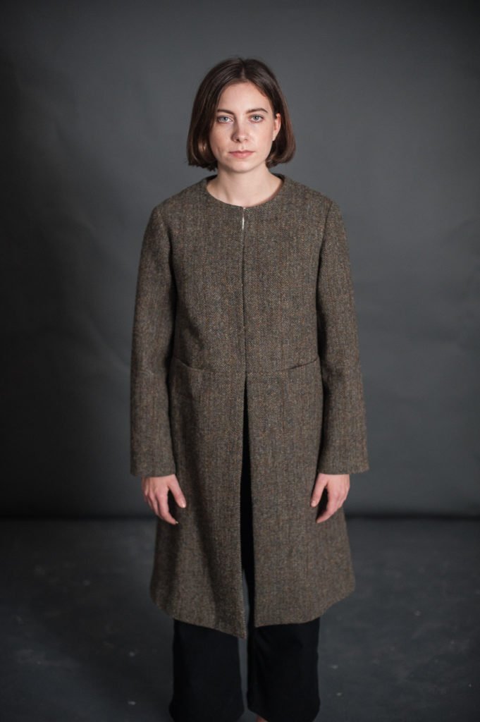 Woman wearing the Strand Coat sewing pattern by Merchant and Mills. A coat pattern made in linen, cotton drill, corduroy, seersucker or wool fabric featuring a hook and eye closure, round neck, long sleeves and a side pocket.