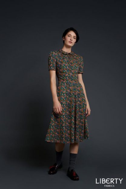 Woman wearing the Bella Tea Dress sewing pattern by Liberty Sewing Patterns. A dress pattern made in cotton, silk or linen fabrics, featuring short sleeves, side zipper closure, bust darts, waist with flared skirt and Peter Pan collar