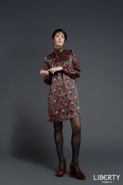 Woman wearing the Bertie Shift Dress sewing pattern by Liberty Sewing Patterns. A dress pattern made in cotton, silk, linen or light velvet fabrics, featuring a high neck, long sleeves with button cuff, back zip closure, relaxed fitting and in-seam pockets.
